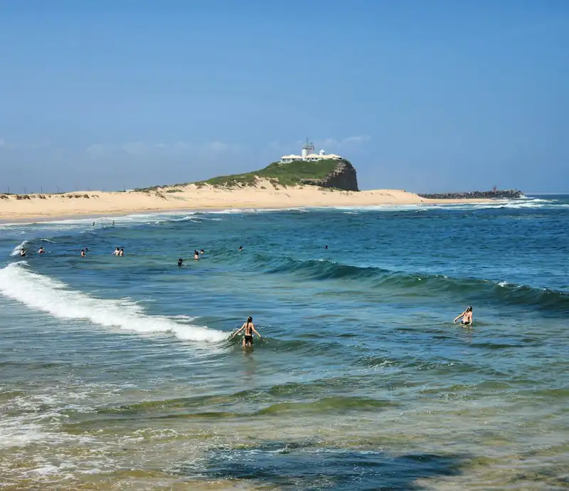 Surfers at Nobbys Beach with the Nobbys Head lighthouse behind